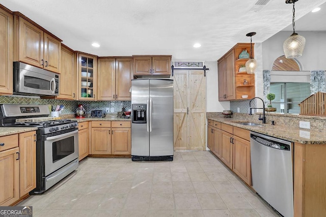 kitchen with a barn door, light stone counters, sink, and stainless steel appliances