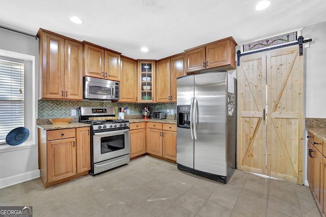 kitchen with appliances with stainless steel finishes, a barn door, tasteful backsplash, and light stone counters