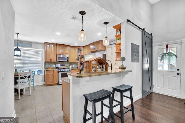 kitchen with kitchen peninsula, appliances with stainless steel finishes, a barn door, and light stone counters