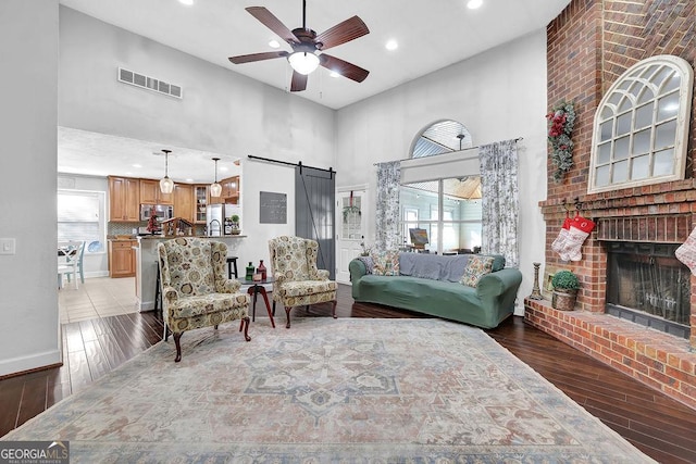 living room with dark hardwood / wood-style flooring, a barn door, ceiling fan, and a high ceiling