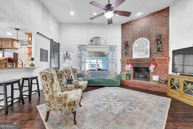 living room featuring ceiling fan, a barn door, brick wall, and a brick fireplace