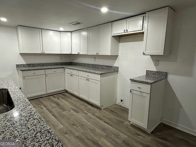 kitchen with sink, hardwood / wood-style flooring, white cabinetry, and light stone counters