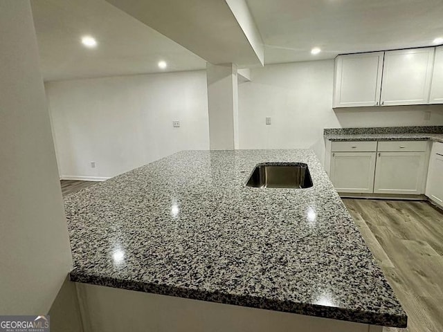 kitchen featuring light wood-type flooring, dark stone counters, white cabinetry, and a peninsula