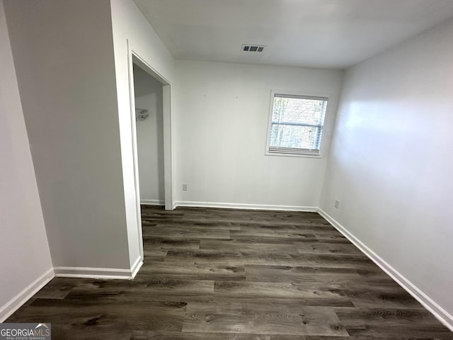 unfurnished room featuring baseboards, visible vents, and dark wood finished floors