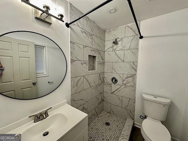 bathroom with a tile shower, vanity, and toilet