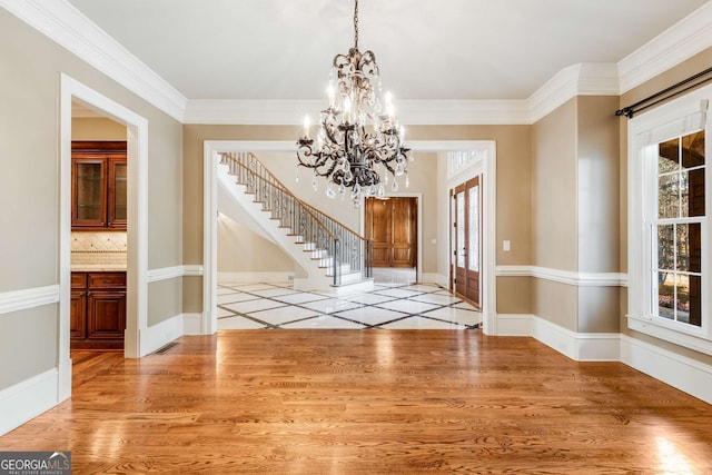 unfurnished dining area featuring light wood-type flooring, ornamental molding, and an inviting chandelier