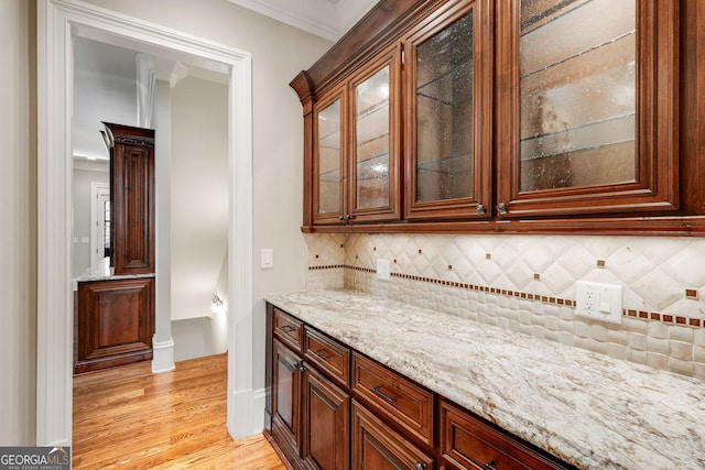 bar featuring light stone countertops, ornamental molding, light wood-type flooring, and tasteful backsplash