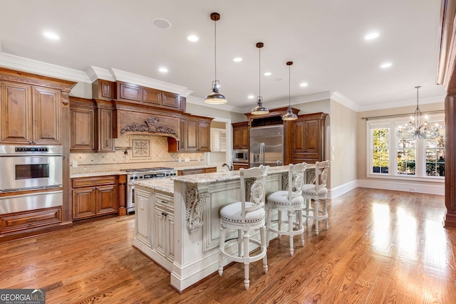 kitchen with pendant lighting, a kitchen island with sink, built in appliances, light stone countertops, and a breakfast bar area