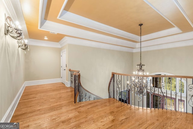 corridor with a raised ceiling, hardwood / wood-style floors, a chandelier, and ornamental molding