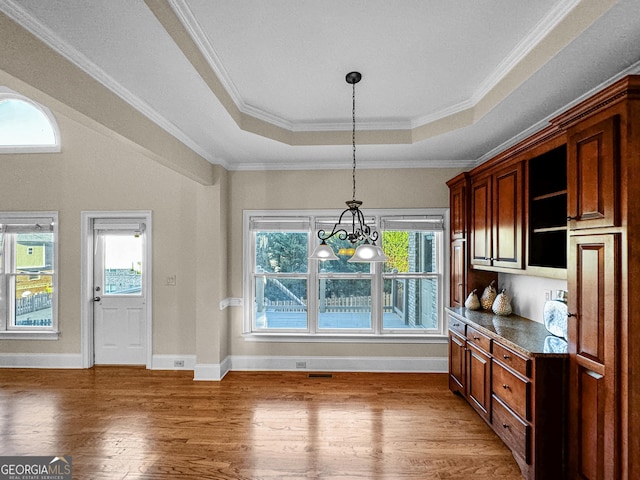 kitchen with pendant lighting, wood-type flooring, ornamental molding, a tray ceiling, and an inviting chandelier