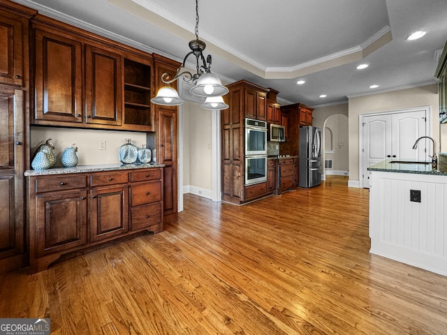 kitchen featuring sink, appliances with stainless steel finishes, light stone counters, a tray ceiling, and decorative light fixtures