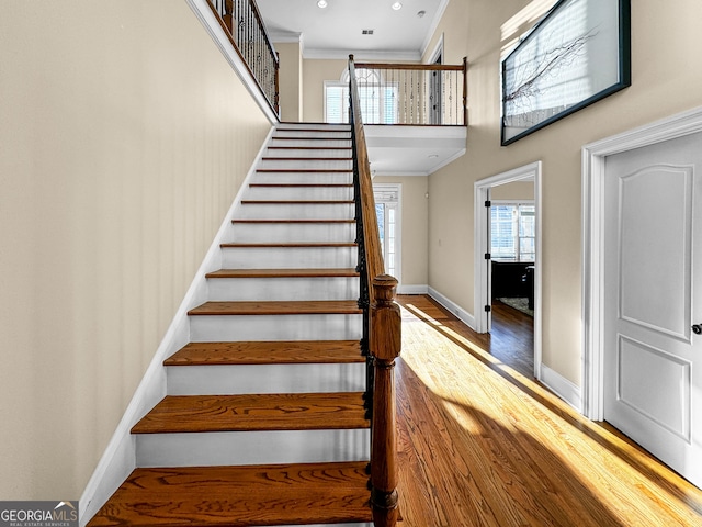 stairs with a high ceiling, crown molding, and hardwood / wood-style floors