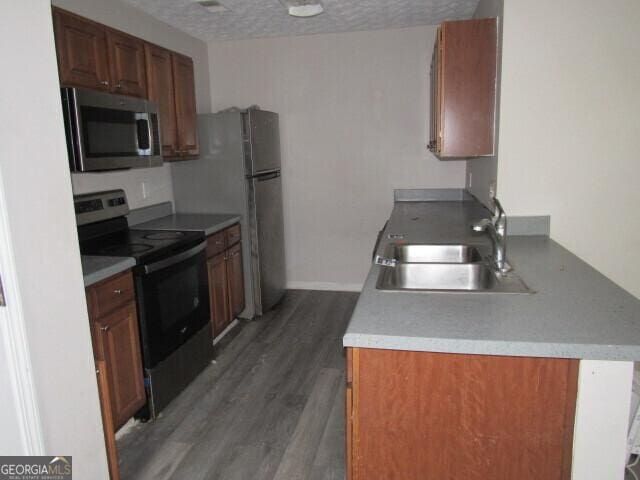 kitchen with wood-type flooring, sink, a textured ceiling, appliances with stainless steel finishes, and kitchen peninsula