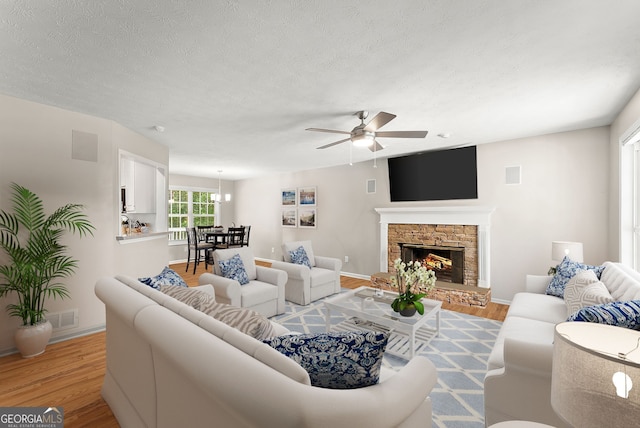 living room featuring a stone fireplace, ceiling fan, light hardwood / wood-style floors, and a textured ceiling