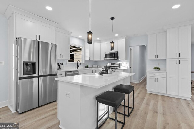 kitchen with white cabinets, appliances with stainless steel finishes, a center island, and hanging light fixtures