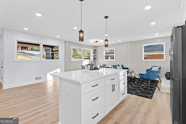 kitchen featuring white cabinetry, stainless steel fridge, pendant lighting, light hardwood / wood-style floors, and a kitchen island