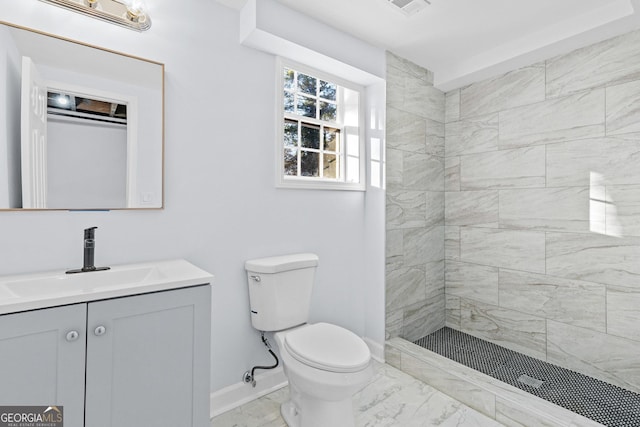 bathroom with a tile shower, vanity, and toilet