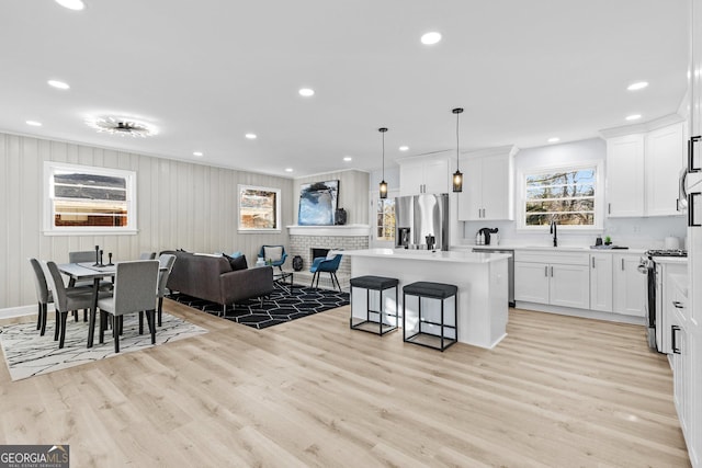 kitchen with pendant lighting, white cabinets, light wood-type flooring, a kitchen island, and stainless steel appliances