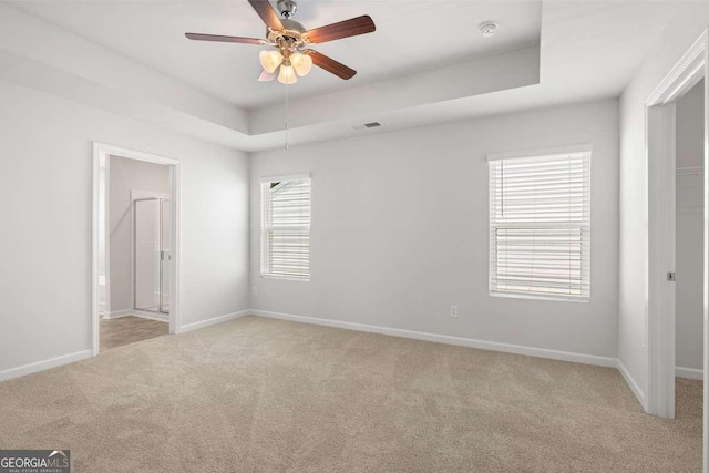 empty room with a tray ceiling, ceiling fan, and light colored carpet