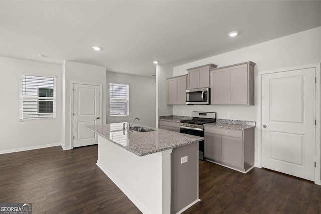 kitchen with light stone counters, stainless steel appliances, a kitchen island with sink, sink, and gray cabinets