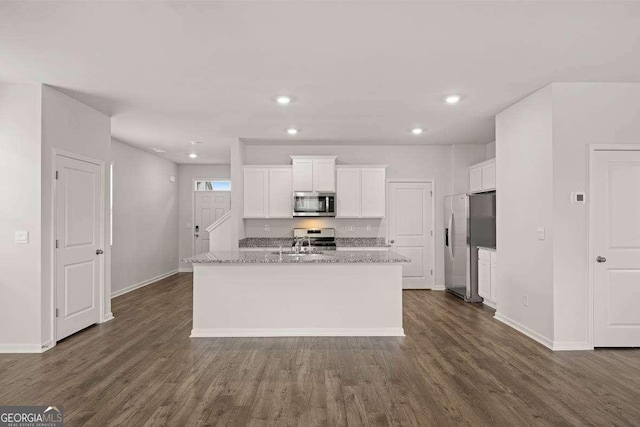 kitchen featuring light stone countertops, stainless steel appliances, white cabinetry, and a kitchen island with sink