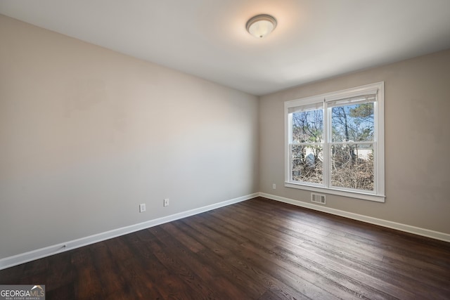 spare room with dark wood-type flooring, visible vents, and baseboards