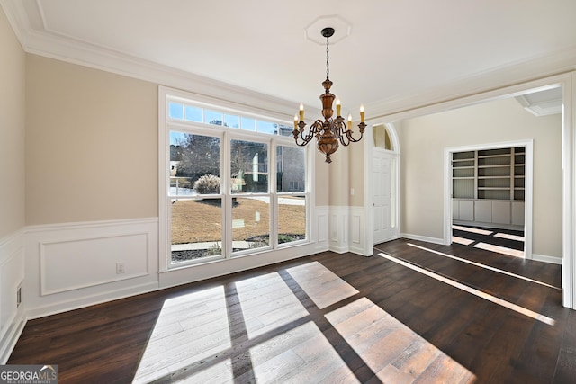 unfurnished dining area with crown molding, dark wood-style flooring, wainscoting, and a notable chandelier