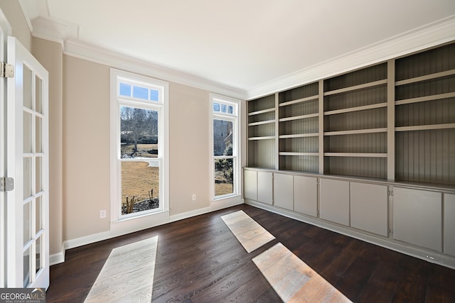 empty room with dark wood-style flooring, crown molding, and baseboards