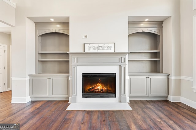 unfurnished living room with a fireplace with flush hearth, built in shelves, baseboards, and dark wood finished floors