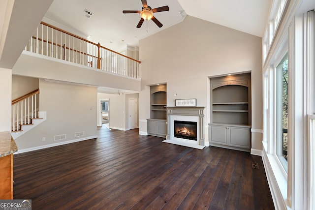 unfurnished living room featuring baseboards, visible vents, dark wood-style flooring, and a glass covered fireplace