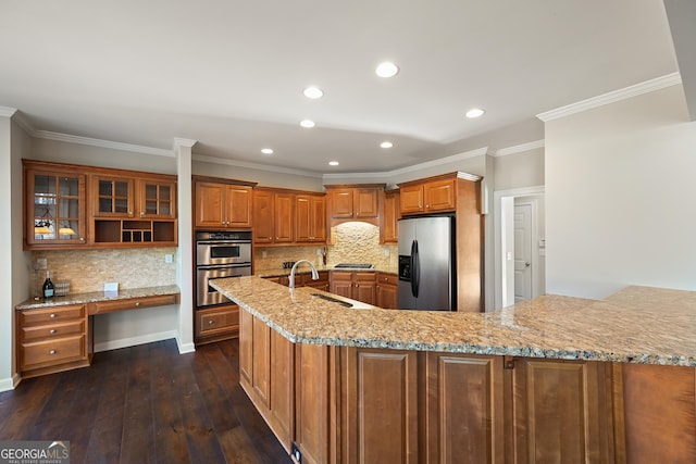 kitchen with light stone counters, brown cabinets, appliances with stainless steel finishes, dark wood-type flooring, and a sink