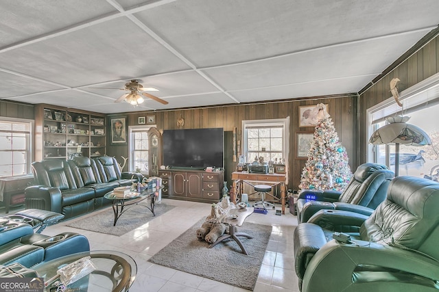 living room featuring built in shelves, light tile patterned floors, ceiling fan, and wood walls