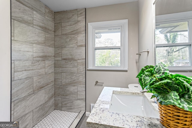 bathroom featuring a tile shower, vanity, and toilet