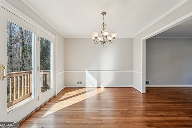 empty room with ornamental molding, a notable chandelier, and hardwood / wood-style floors