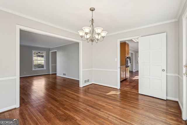 spare room featuring dark hardwood / wood-style floors, crown molding, and a notable chandelier