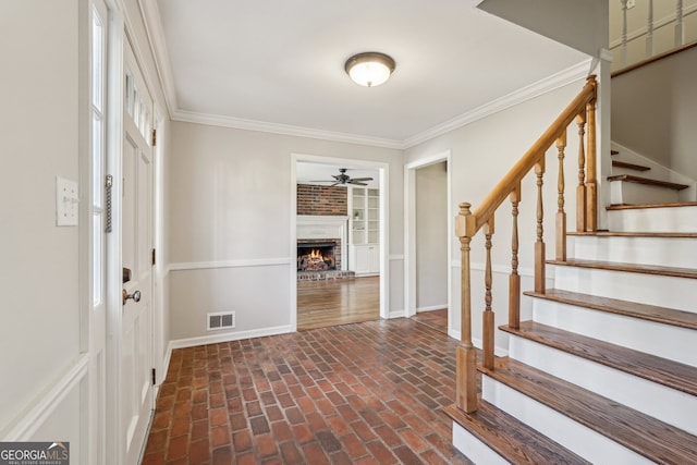 entryway with ceiling fan, ornamental molding, and a brick fireplace