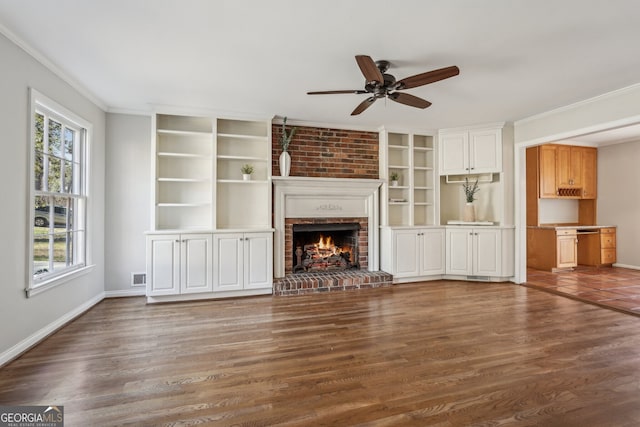 unfurnished living room with wood-type flooring, a brick fireplace, ceiling fan, and ornamental molding