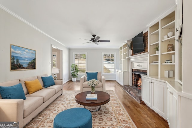 living room with ceiling fan, built in features, crown molding, a fireplace, and hardwood / wood-style flooring