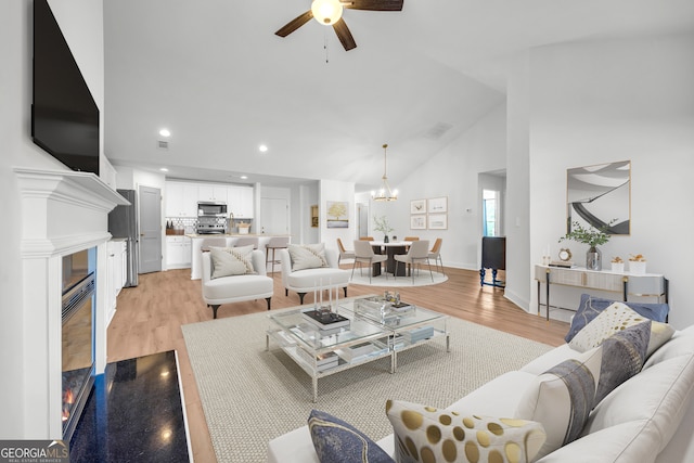 living room featuring ceiling fan with notable chandelier, light hardwood / wood-style flooring, and lofted ceiling