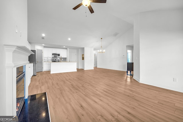 unfurnished living room featuring vaulted ceiling, ceiling fan with notable chandelier, and light wood-type flooring