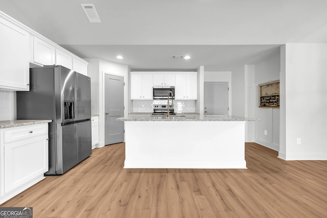 kitchen featuring decorative backsplash, white cabinets, a center island with sink, and stainless steel appliances