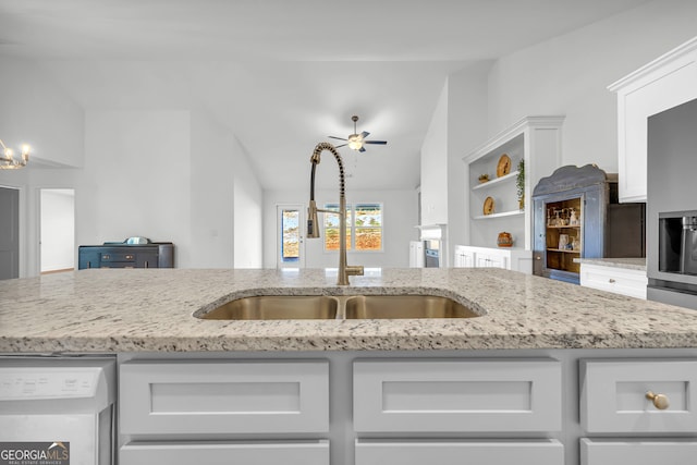 kitchen featuring ceiling fan with notable chandelier, dishwasher, white cabinetry, sink, and light stone counters