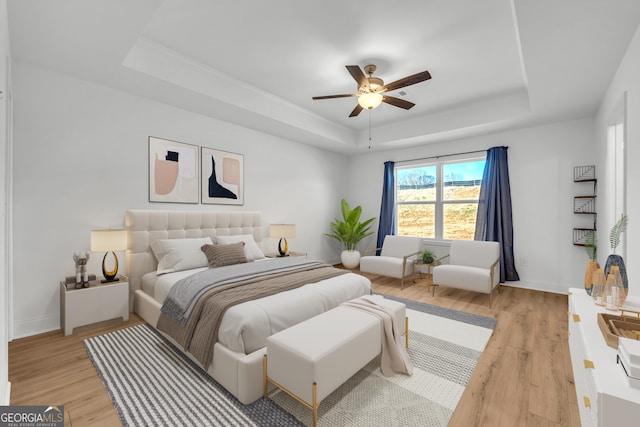 bedroom with ceiling fan, light hardwood / wood-style flooring, and a raised ceiling