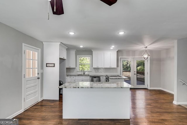 kitchen with white cabinets, a kitchen island, light stone counters, and dishwasher