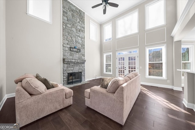 living room featuring french doors, ceiling fan, dark wood-type flooring, a fireplace, and a high ceiling