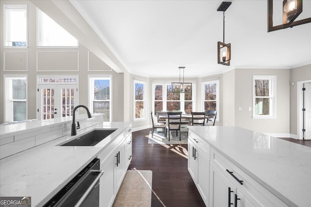 kitchen featuring white cabinets, light stone counters, sink, dishwasher, and hanging light fixtures