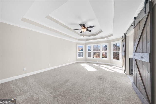 carpeted empty room with a barn door, a raised ceiling, ceiling fan, and ornamental molding