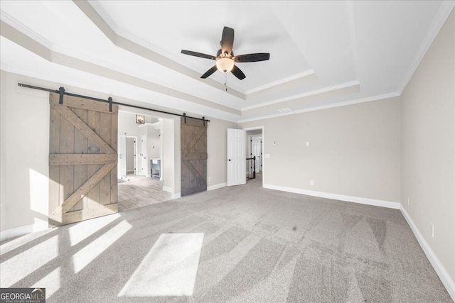 carpeted empty room featuring ceiling fan, a barn door, a raised ceiling, and ornamental molding