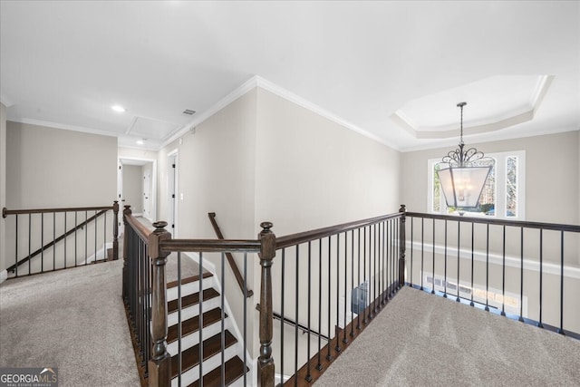 hallway with a raised ceiling, crown molding, carpet, and a chandelier