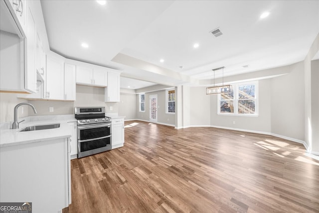 kitchen with stainless steel range with electric stovetop, a tray ceiling, sink, white cabinets, and plenty of natural light